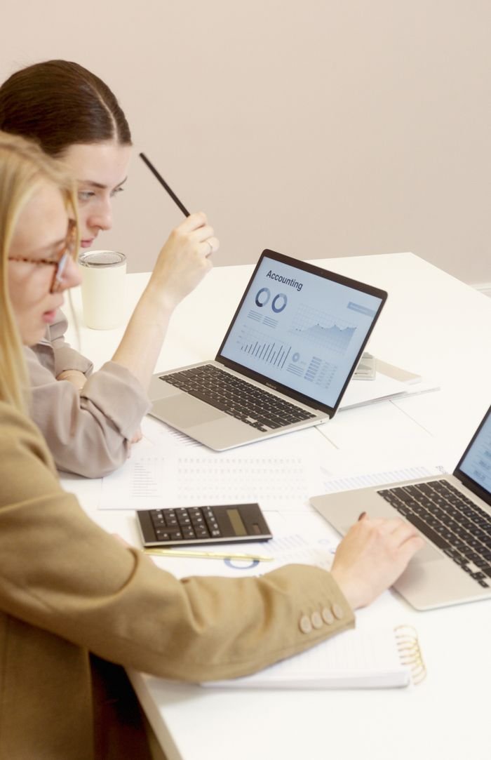Offerings Two women collaborate on financial data analysis with laptops in an office setting.